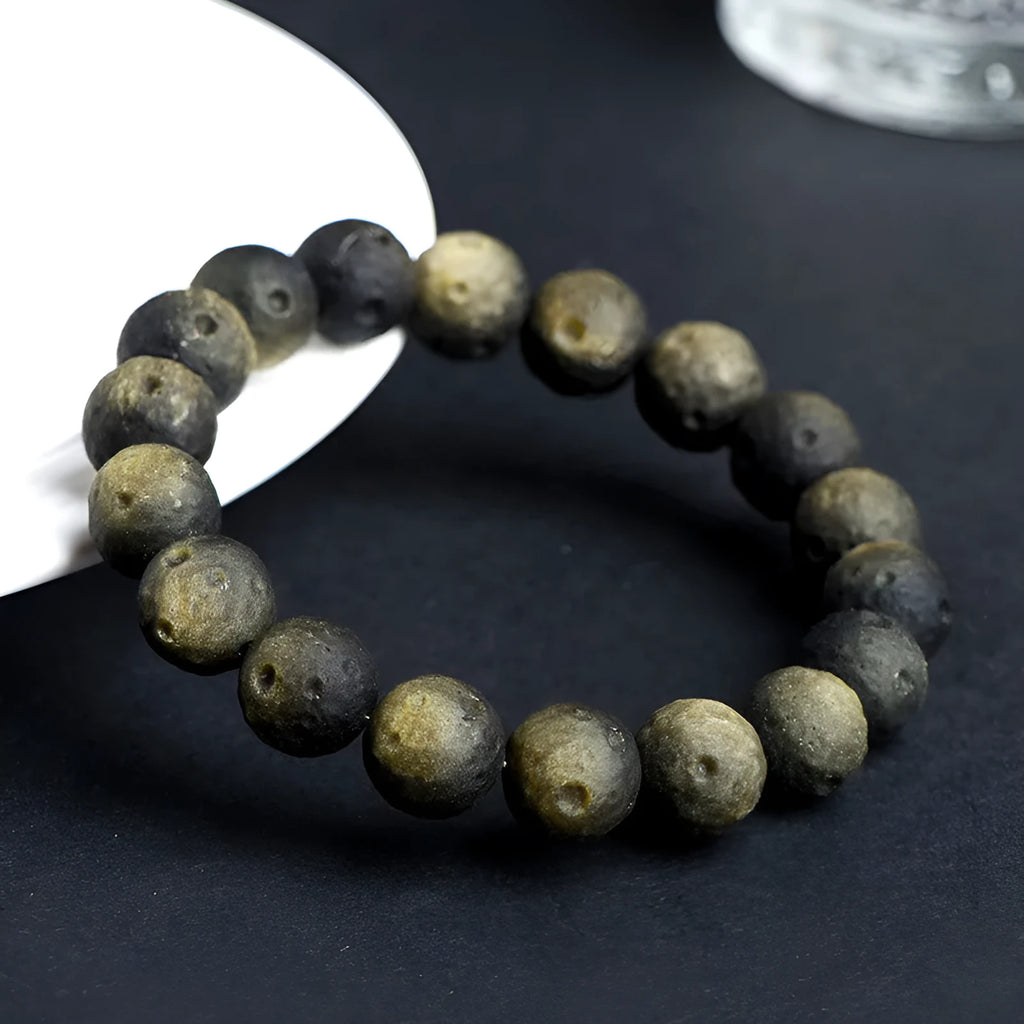 Natural obsidian crater ball bracelet in gold or silver stone colour on a wrist, showing textured bead surface.