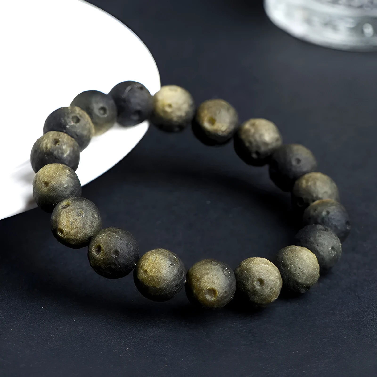 Natural obsidian crater ball bracelet in gold or silver stone colour on a wrist, showing textured bead surface.