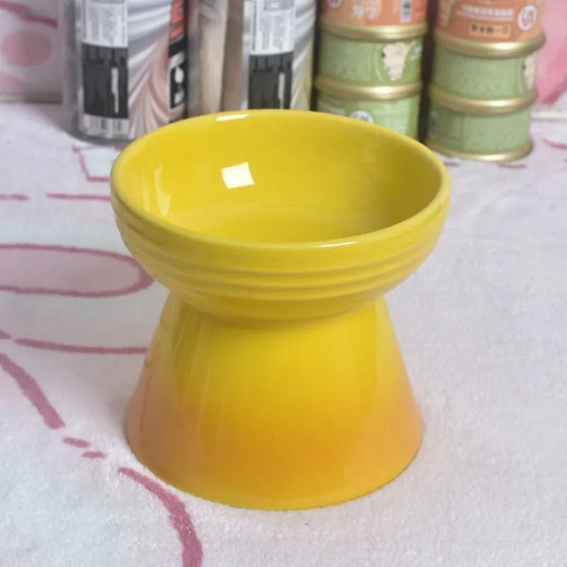 A high-footed white ceramic pet bowl with a slanted rim and non-slip black base, shown on a wooden floor.