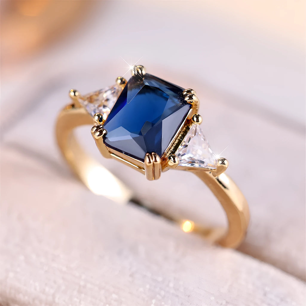 Gold and sapphire blue rectangular copper ring for women on a plain background.
