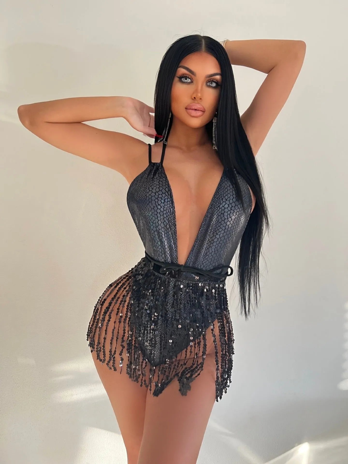 A gold backless one-piece swimsuit with tassel detailing on a mannequin, showing a form-fitting silhouette.