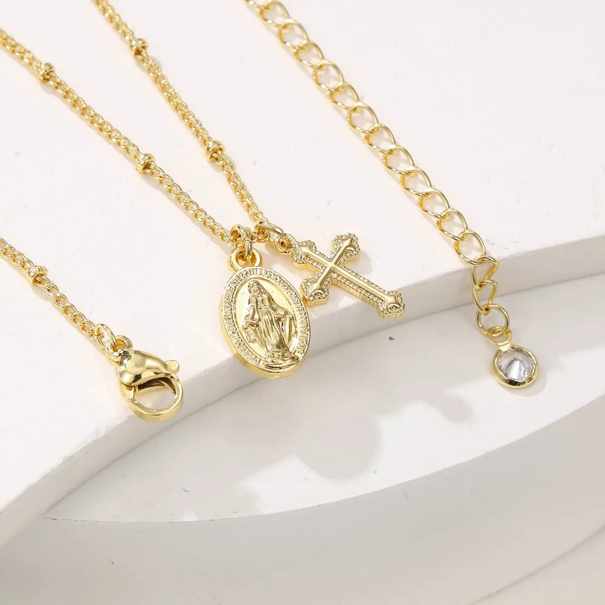 Geometric gold cross Virgin Mary pendant necklace on a chain with a lobster clasp.