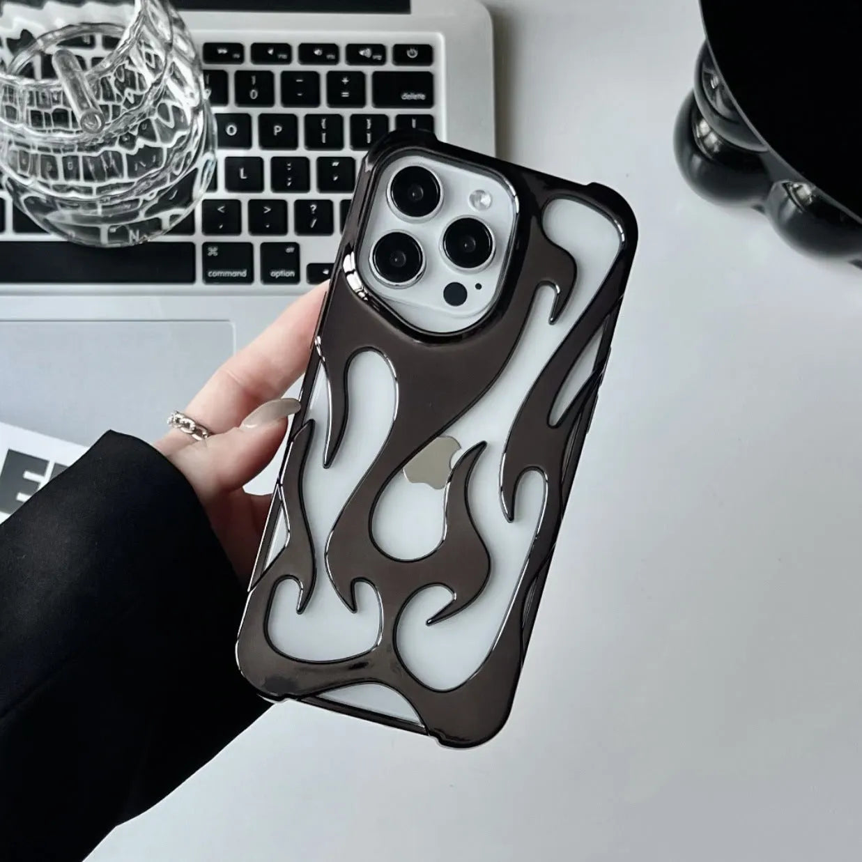 Electroplated hollow flame pattern phone case for iPhone on a table, showing silver metallic finish and cut-out design.