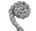 Braided knot style crib bumper in spandex velvet, wrapped around white cot rails in a nursery.