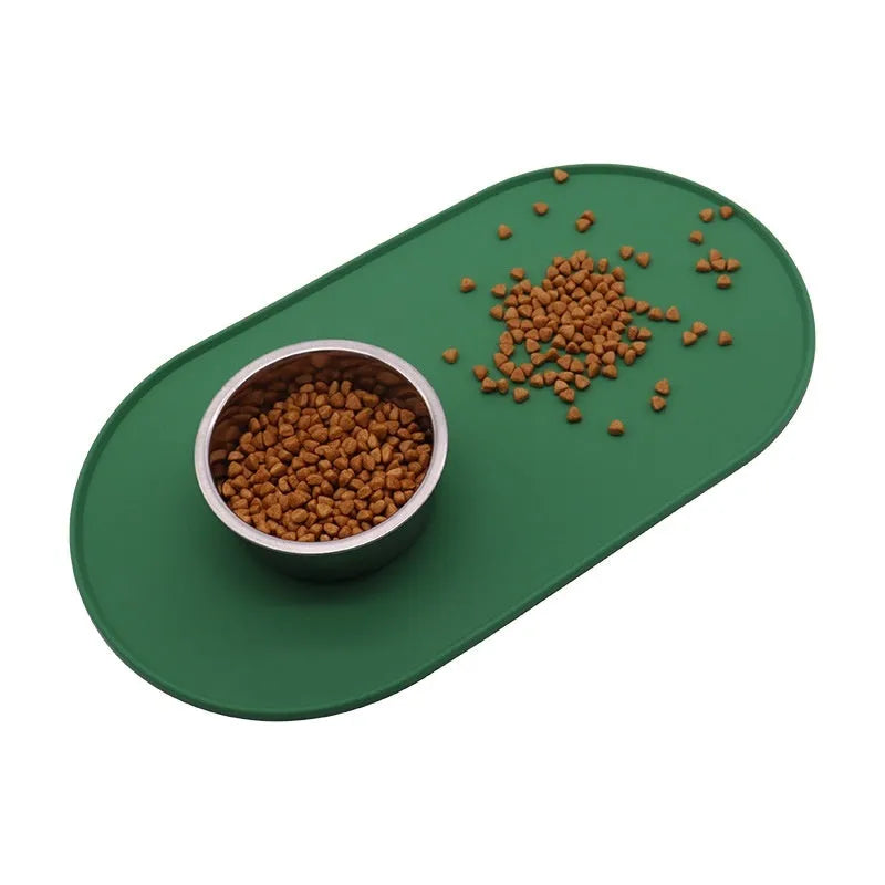 Beige silicone cat feeding mat with raised edge containing a food bowl and scattered kibble on a kitchen floor.