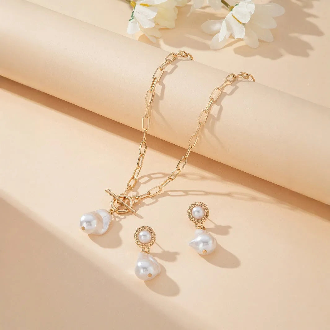 Gold-toned baroque pearl pendant necklace and matching stud earrings set on a dark background.