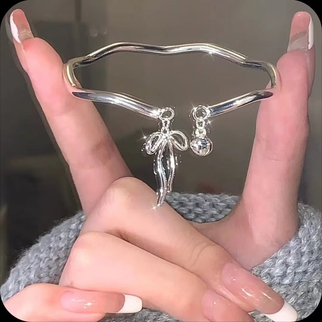 Silver toned adjustable bracelet with bow bell charm on a wrist, showing lobster clasp.