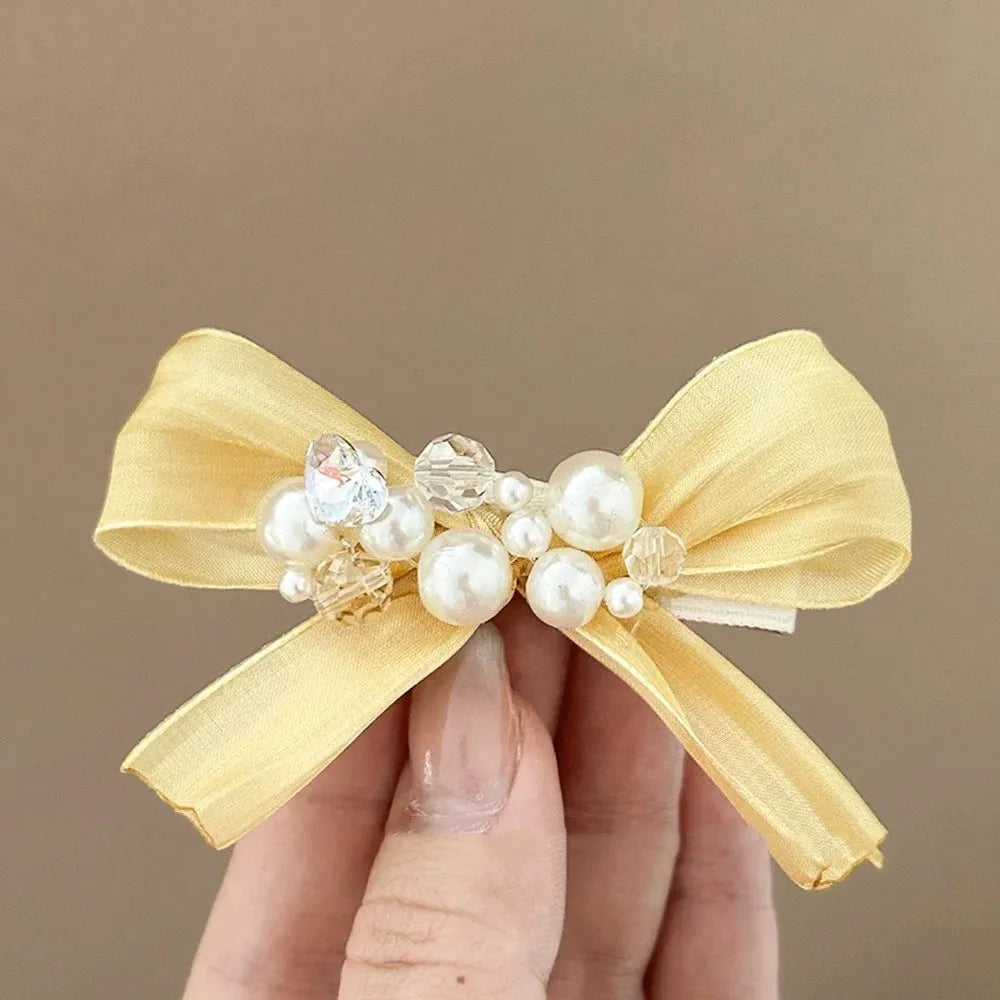 Yellow cloth bow barrette with rhinestones and a pearl on a plastic duckbill hair clip.