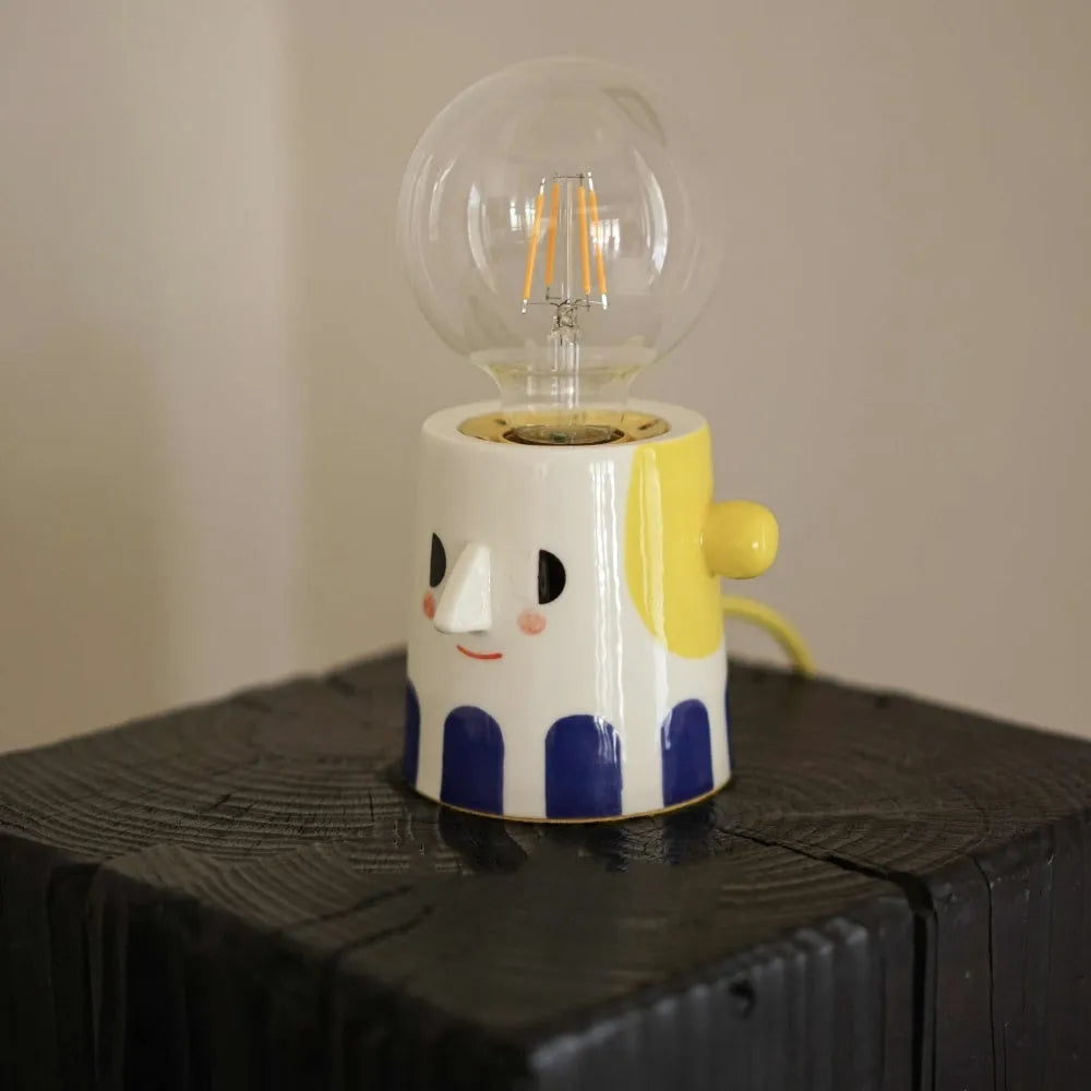 Handmade solid ceramic table lamp with spherical white shade on a wooden surface, showing UK plug.