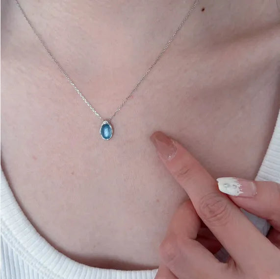 Close-up of a navy blue water drop pendant necklace with a platinum-colour finish on a textured cross chain.
