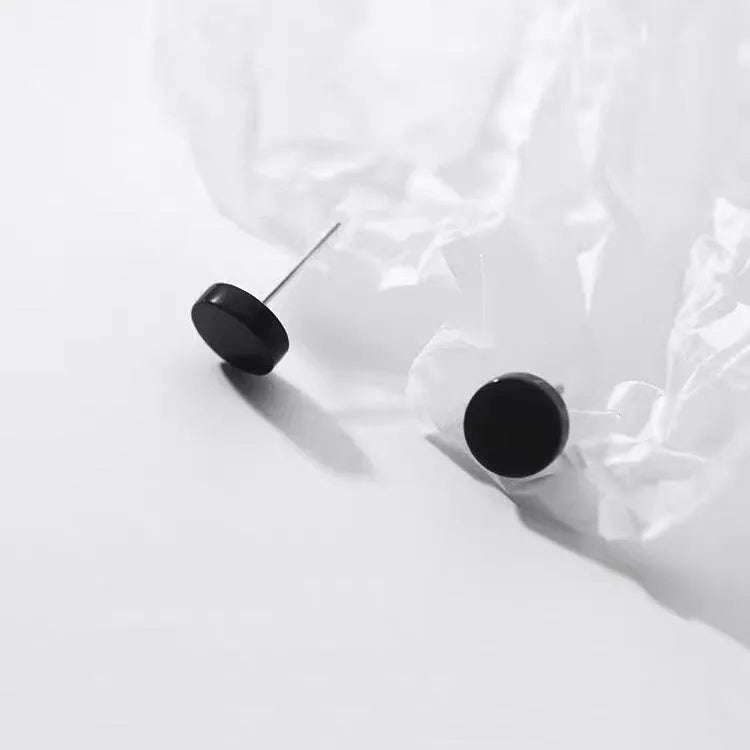 A pair of simple round flat stud earrings in sterling silver, shown in silver and black finishes.