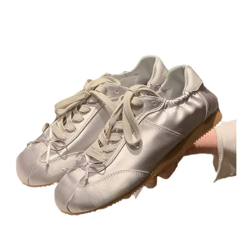 Women's champagne pink satin ballet flat shoes with a round toe and white front lace-up detail.