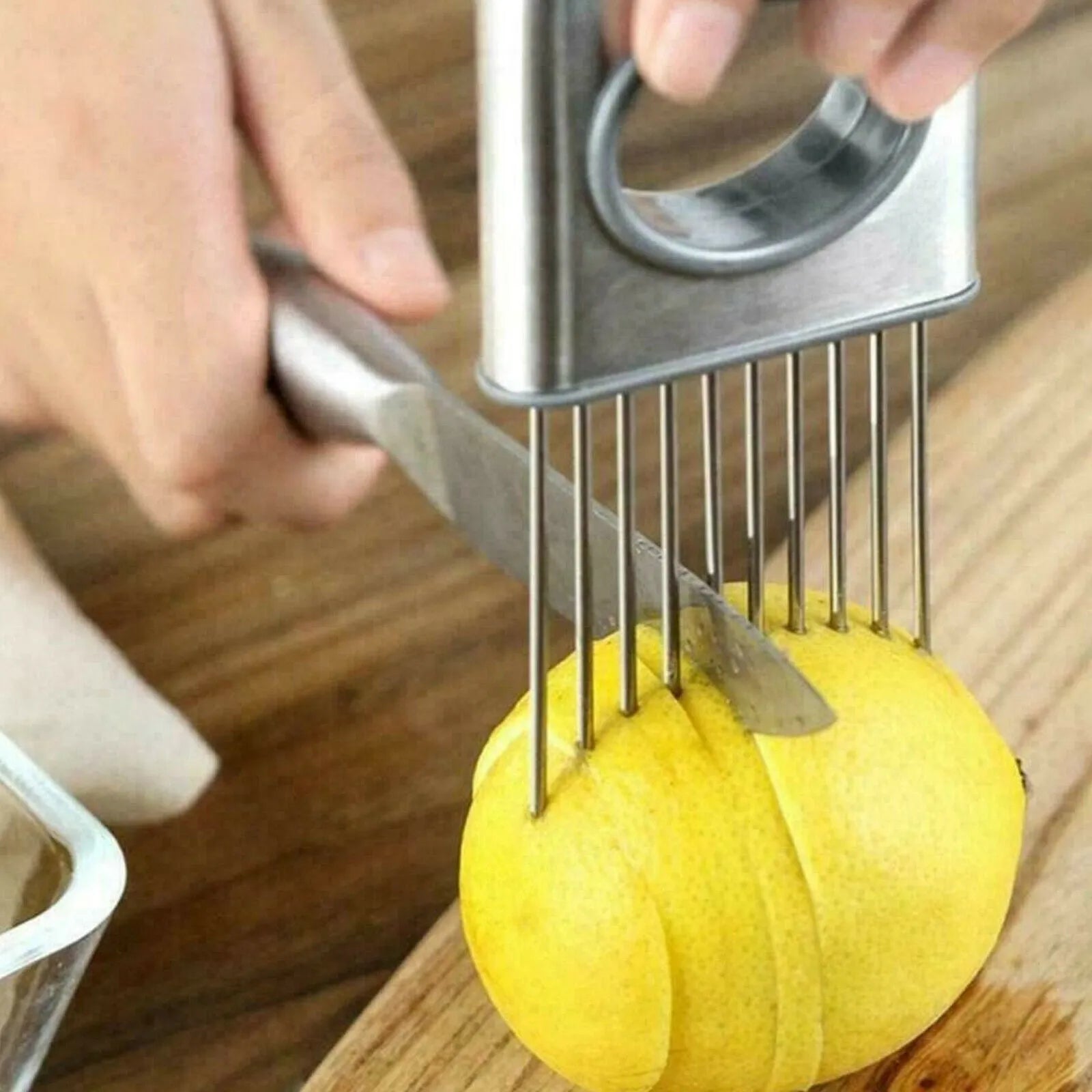 Stainless steel onion holder kitchen tool with sharp prongs and a red finger guard protector on a cutting board.
