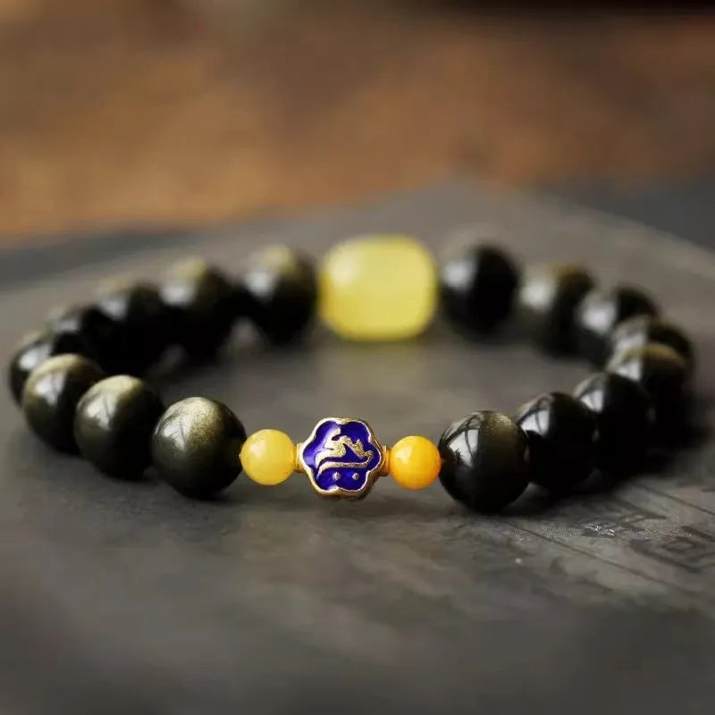 Golden obsidian bracelet with geometric beads and a detailed zodiac animal charm on a wrist.