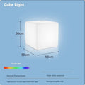 A modern square white LED cube light stool in a garden setting, showing its size options.