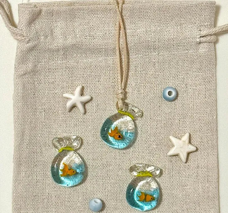 Women's necklace with a blue hand-painted fish charm on a beige cotton and linen clavicle chain.