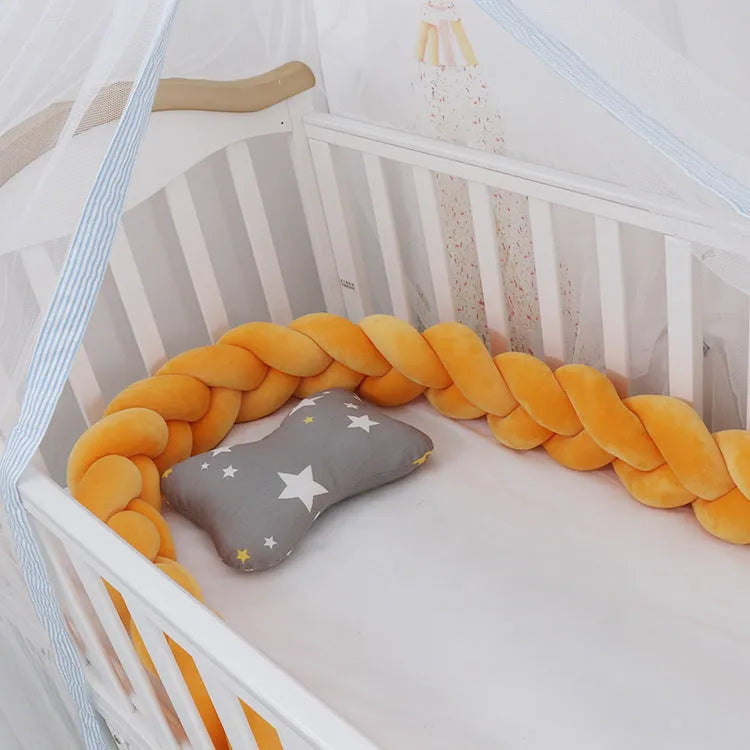 Braided knot style crib bumper in spandex velvet, wrapped around white cot rails in a nursery.