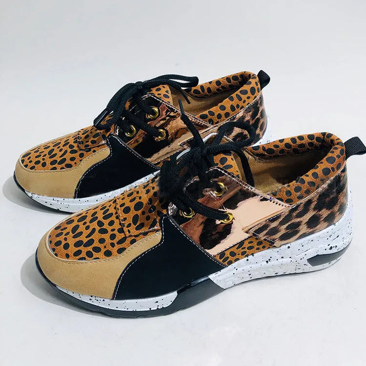 Women's black suede wedge sneakers with a low-cut ankle and round toe on a wooden floor.