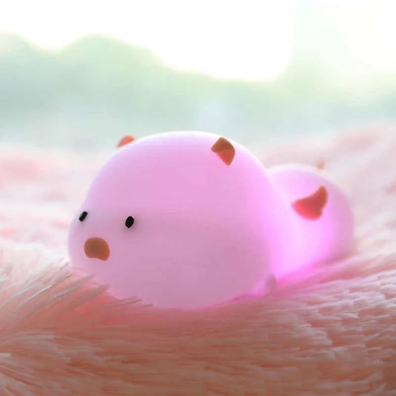 Pink silicone night light in the shape of a sleeping pig on a table.