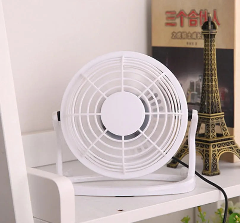 Compact black mini USB desk fan with adjustable tilt on a desk next to a laptop.