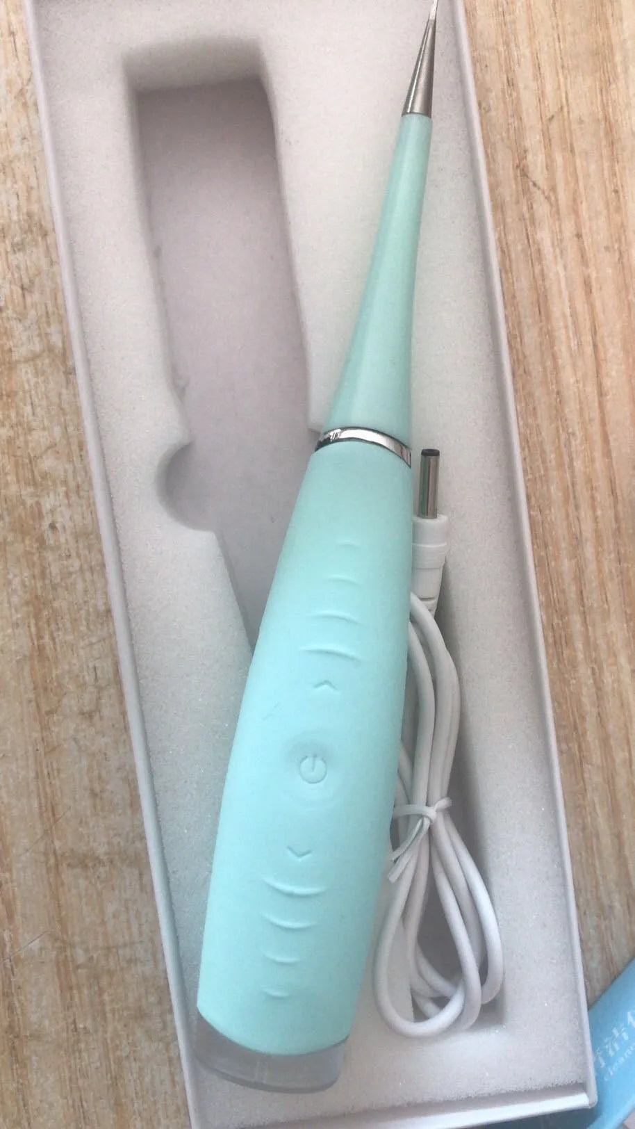 Pink and blue waterproof electric dental scaler tool on a bathroom counter with charging cable.
