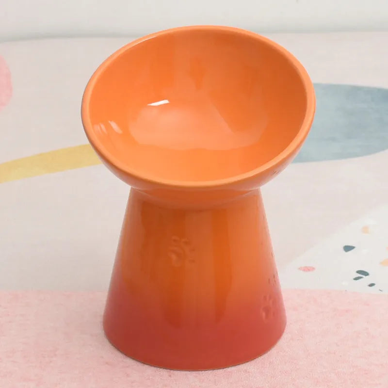 A high-footed white ceramic pet bowl with a slanted rim and non-slip black base, shown on a wooden floor.