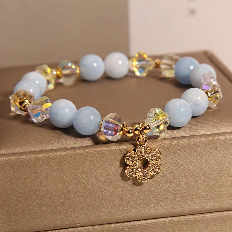 Women's aquamarine crystal bracelet with a four-leaf clover charm and pearl accent on wrist.