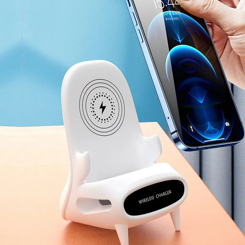 White mini chair-shaped wireless phone charger on a desk, with phone seated on it.