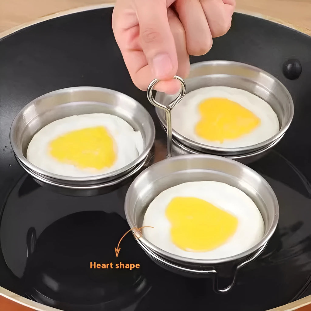 Mini heart-shaped and round stainless steel egg steamer with cooker base on a kitchen counter.