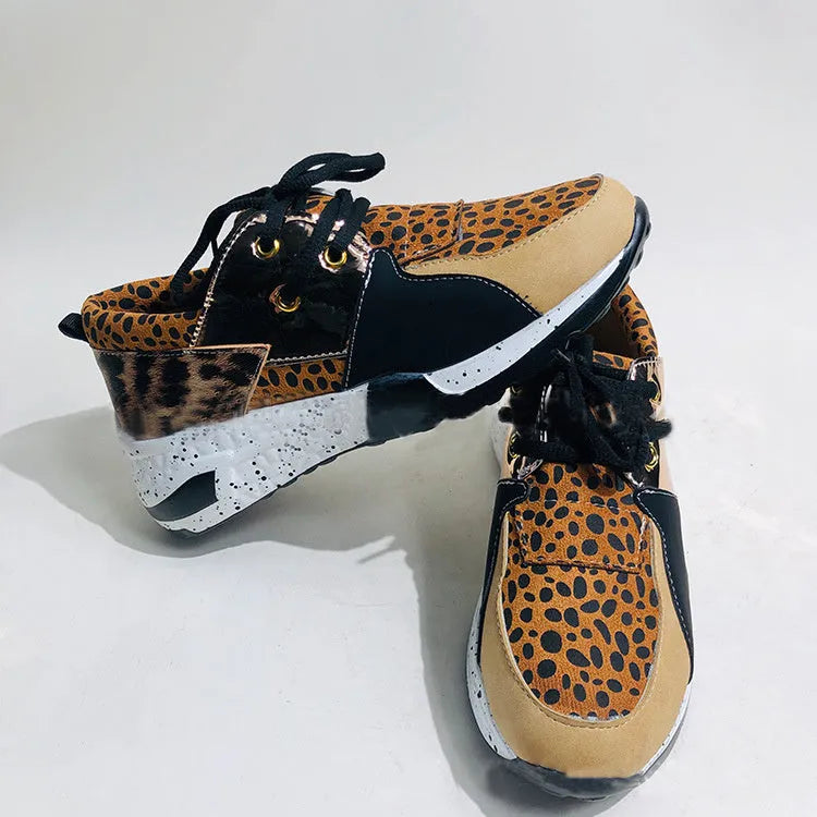 Women's black suede wedge sneakers with a low-cut ankle and round toe on a wooden floor.