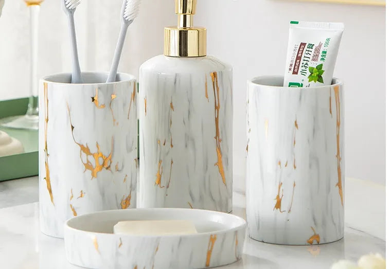 White ceramic bathroom wash kit set with two cups, a soap dish, and a bottle on a marble background.