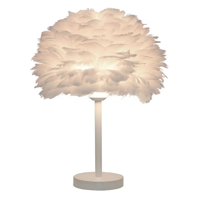 Handmade feather table lamp with metal base, white feathers, and remote control on a wooden bedside table