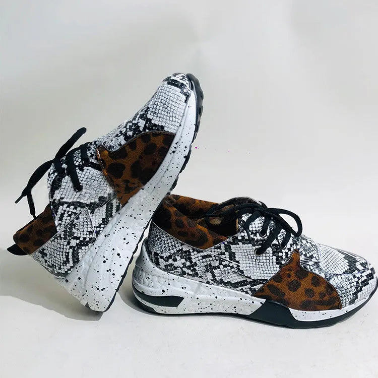 Women's black suede wedge sneakers with a low-cut ankle and round toe on a wooden floor.