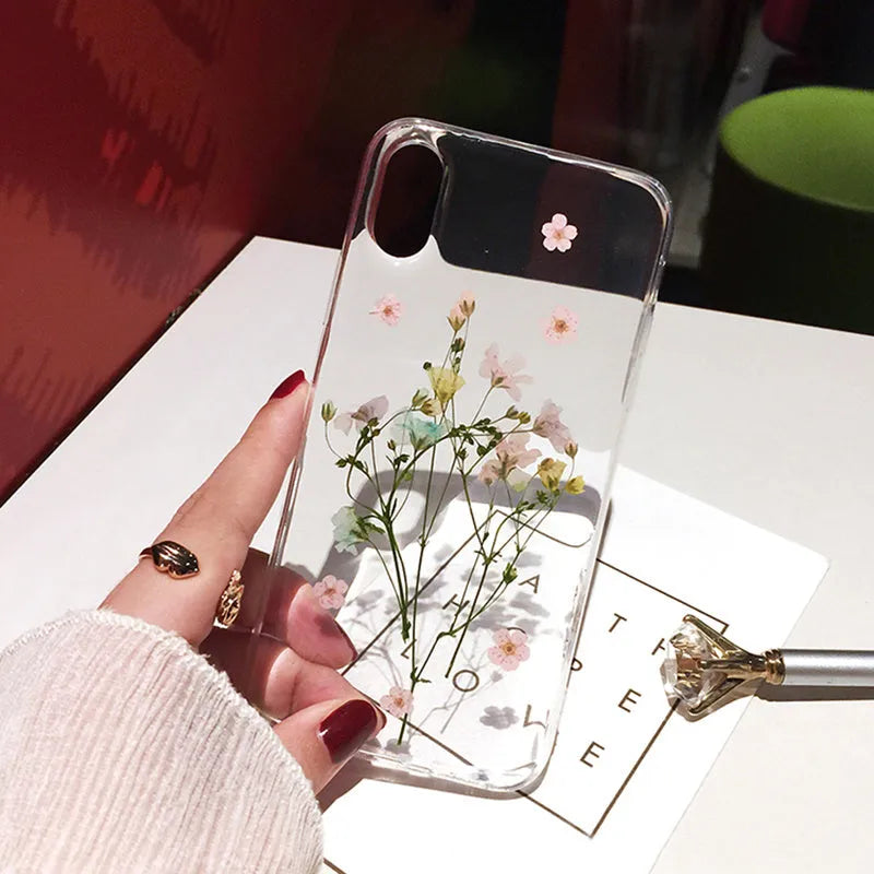 Clear TPU iPhone case showing real pink dried flowers encapsulated in epoxy resin on the back.