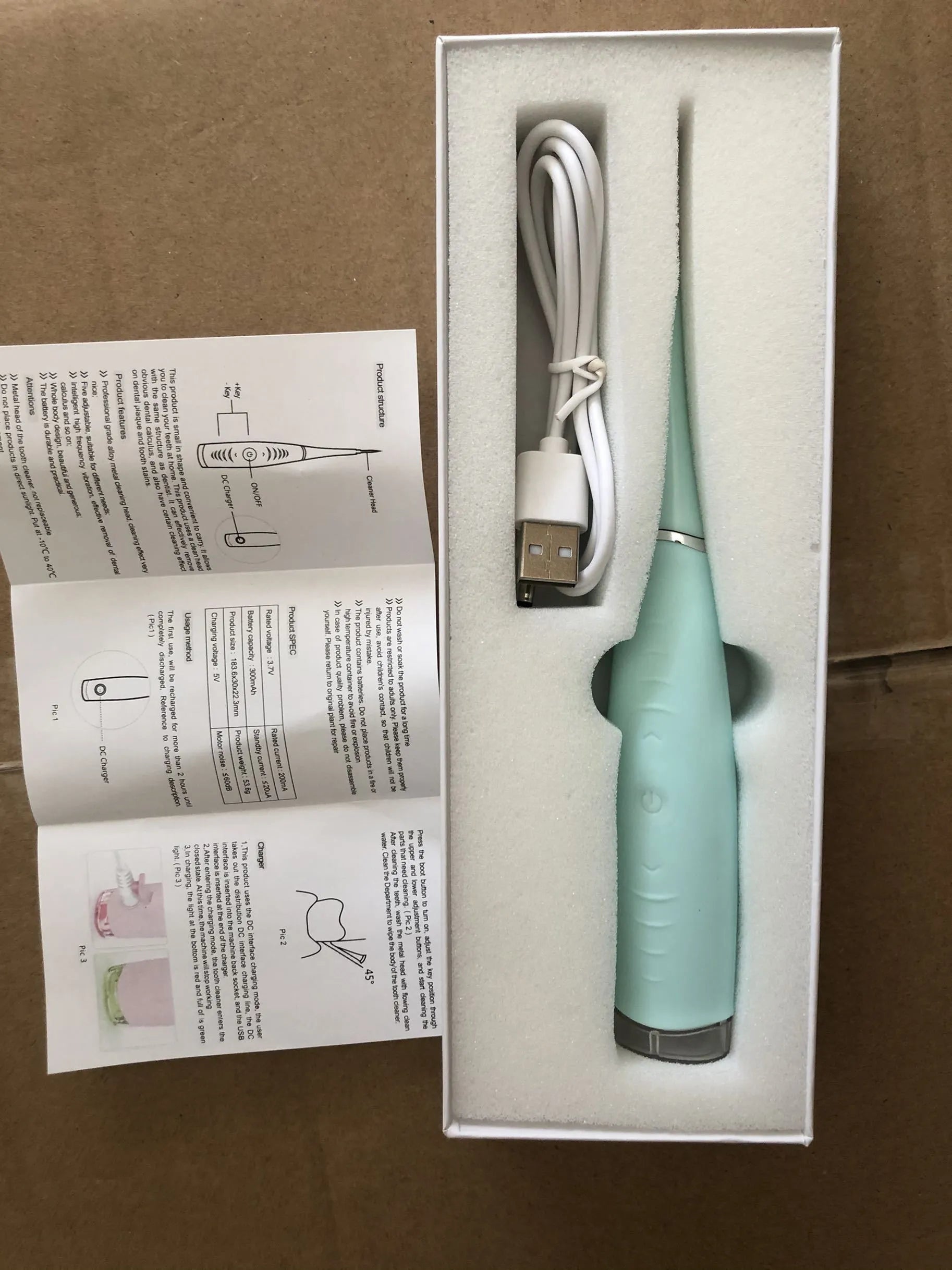 Pink and blue waterproof electric dental scaler tool on a bathroom counter with charging cable.