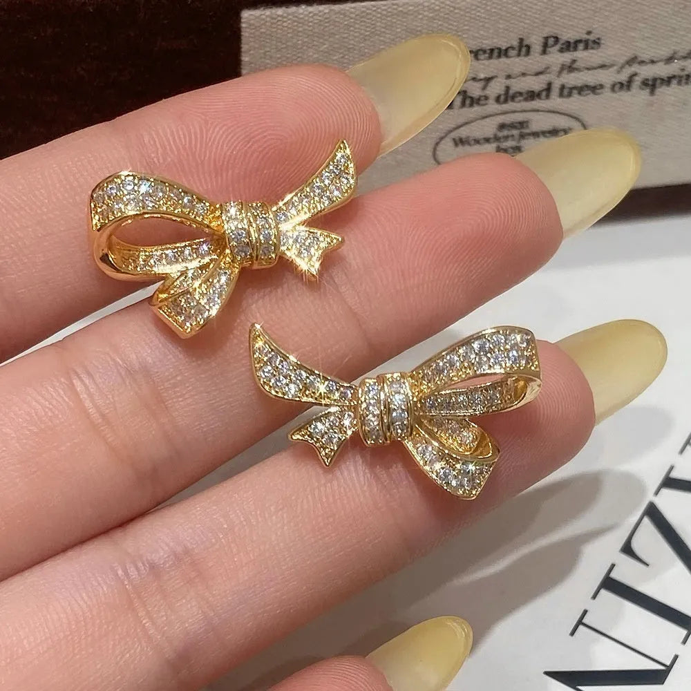 Gold electroplated bowknot ear studs with miniature zircon inlay and 925 silver needle on white background