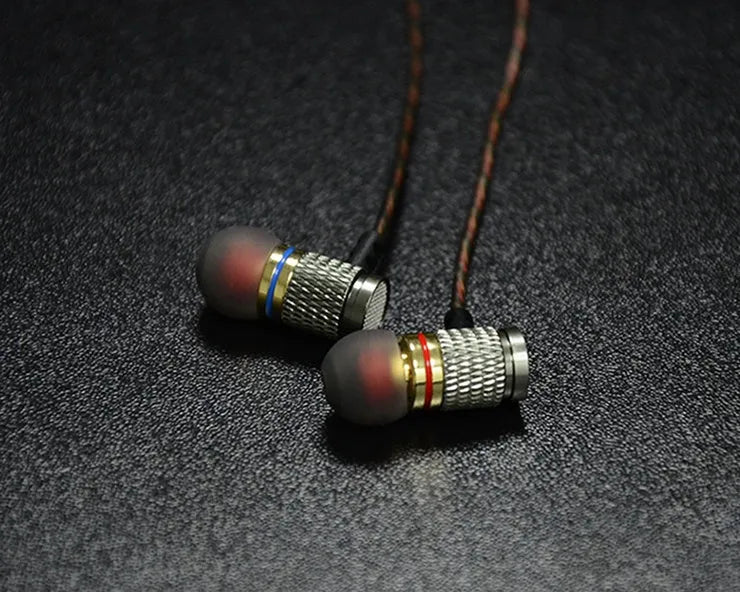 Close-up of wired in-ear headphones with metal subwoofer, TPE earplugs, and a 3.5mm L-bend plug on a silicone cable.