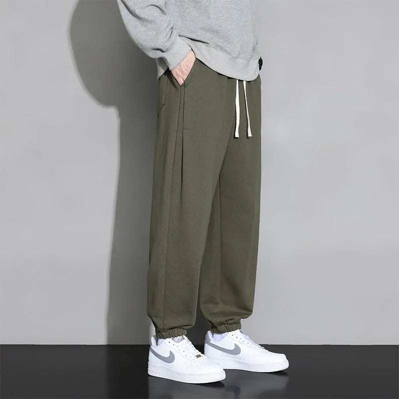 Men's loose grey cotton blend sports trousers with a drawstring waist on a hanger.