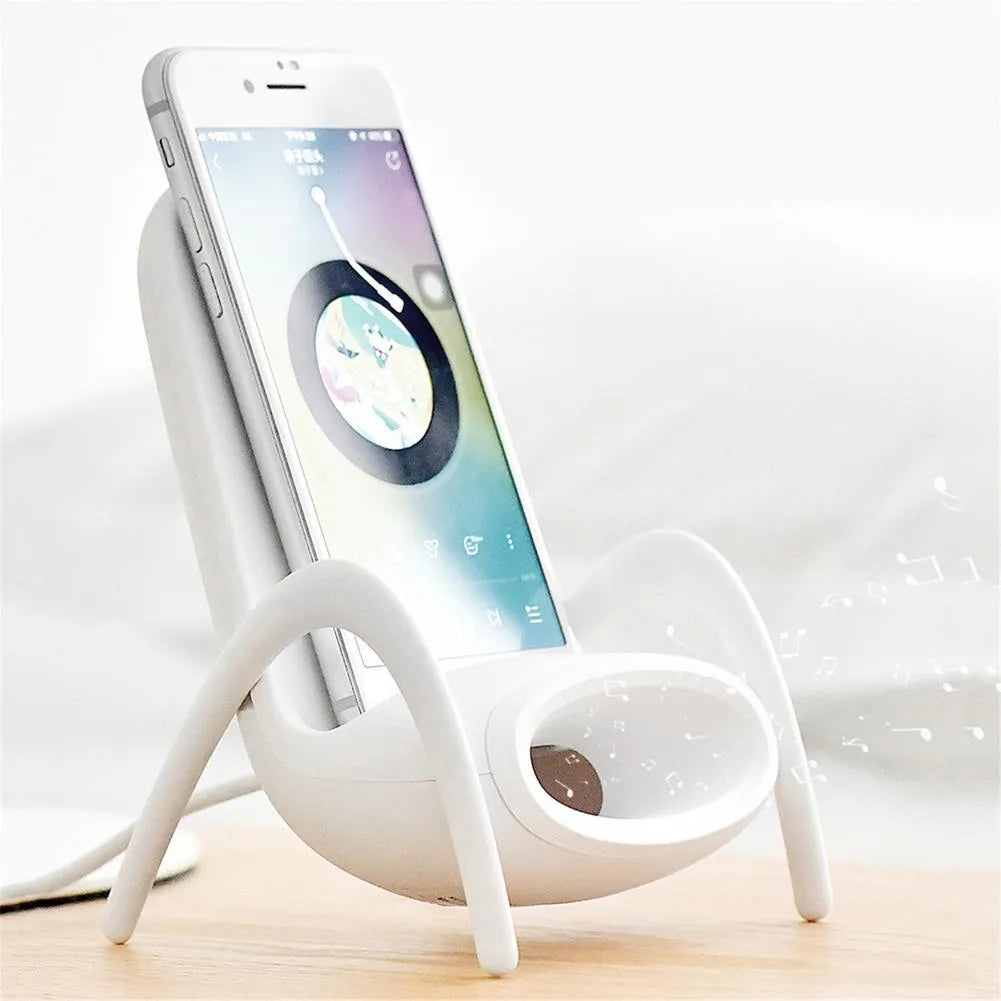 White mini chair-shaped wireless phone charger on a desk, with phone seated on it.