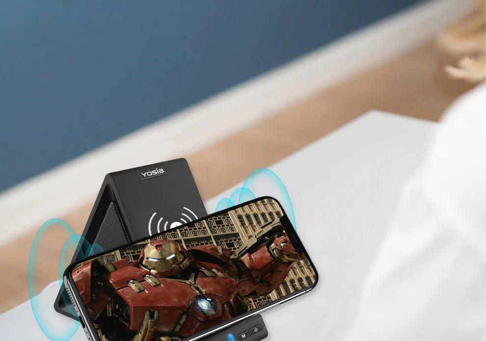 Black multifunctional power bank with integrated Bluetooth speaker and wireless charging phone stand on a desk.