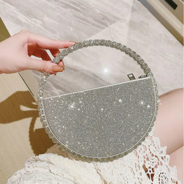 Round silver white PU evening bag with rhinestone details and crossbody strap on flat surface