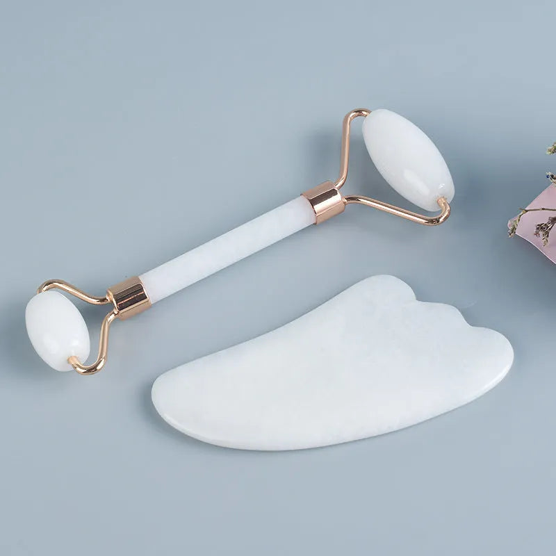 White jade facial roller and gua sha scraping board set on a table.