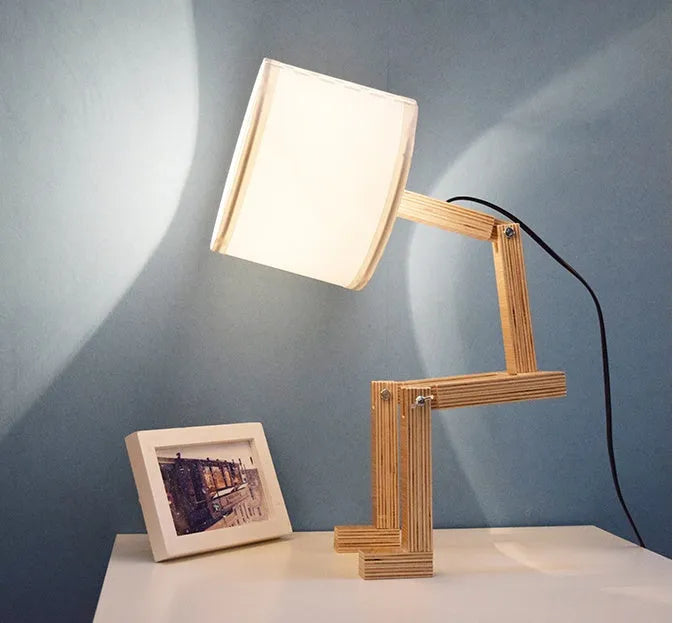 Creative humanoid wooden table lamp with white fabric shade and deformable design on a wooden surface