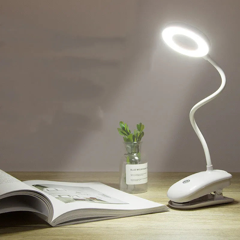 Modern clip-on rechargeable LED desk lamp with touch switch and plastic shade in use on a desk.