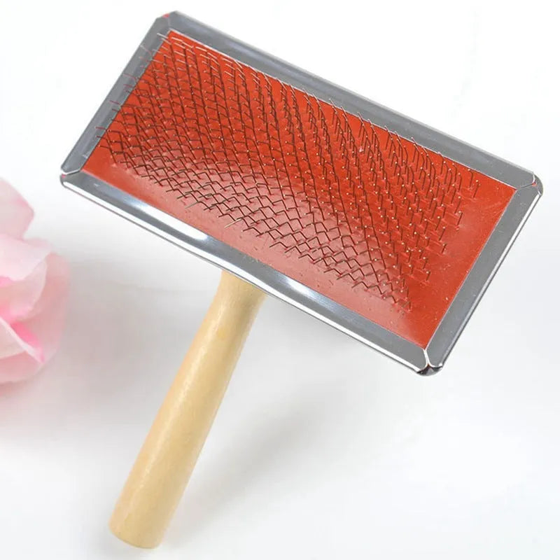 Red pet needle comb with wooden handle and stainless steel pins on a grooming surface