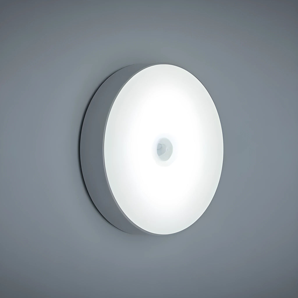 Small round white motion sensor night light with USB charging cable and adhesive tape.