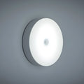 Small round white motion sensor night light with USB charging cable and adhesive tape.