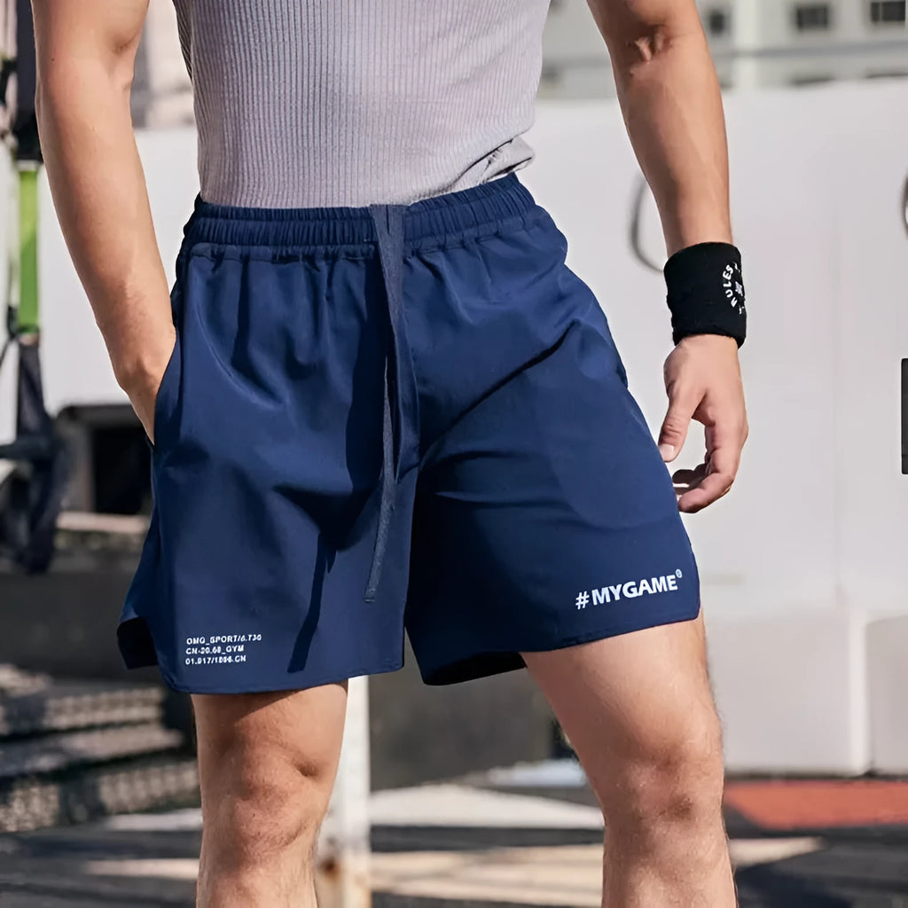 Man wearing grey elastic training shorts in a gym setting, demonstrating the short-length, quick-dry design.