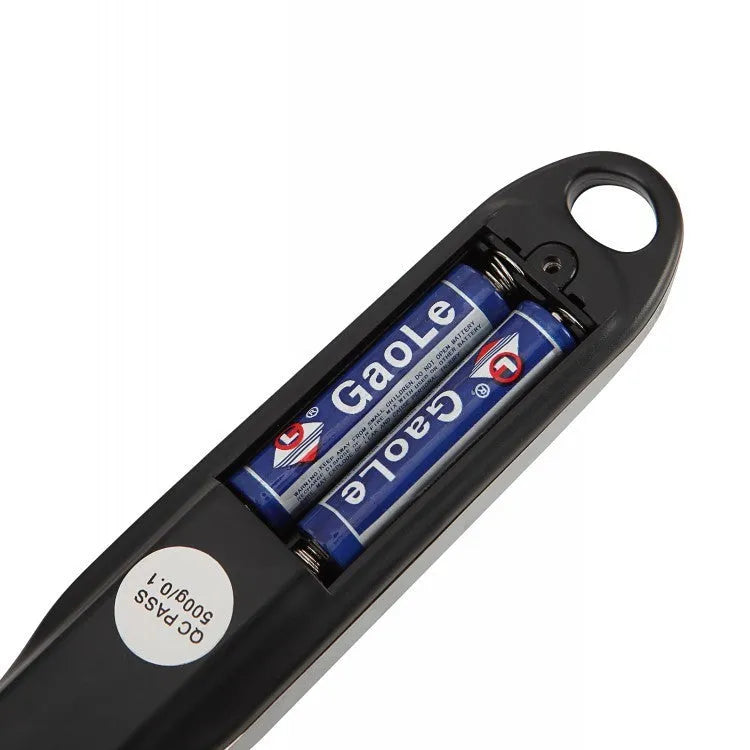 Digital smart measuring spoon with electronic display showing weight, placed on a kitchen worktop.