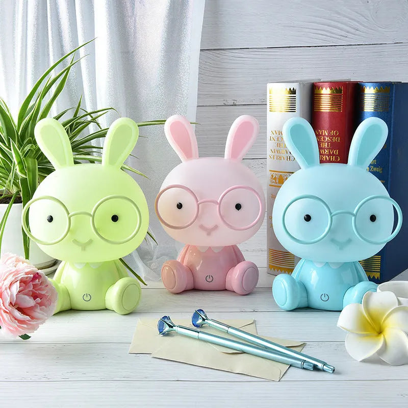 Blue plastic USB cartoon night light with a cute rabbit decoration wearing glasses on a desk.